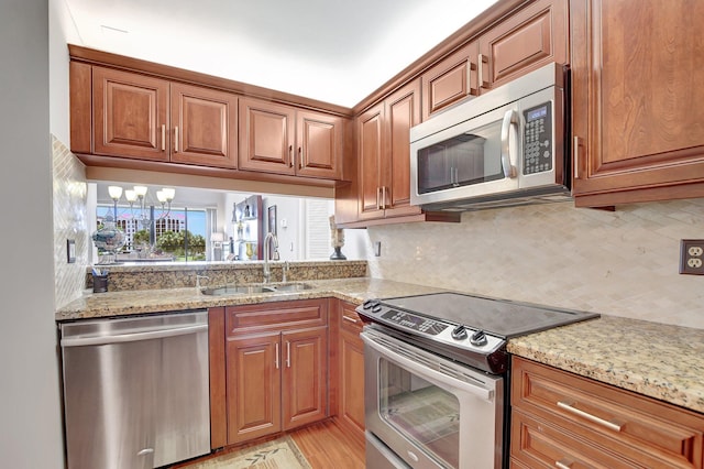 kitchen featuring appliances with stainless steel finishes, an inviting chandelier, sink, backsplash, and light stone countertops