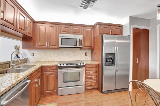 kitchen featuring tasteful backsplash, stainless steel appliances, sink, light stone countertops, and light hardwood / wood-style flooring