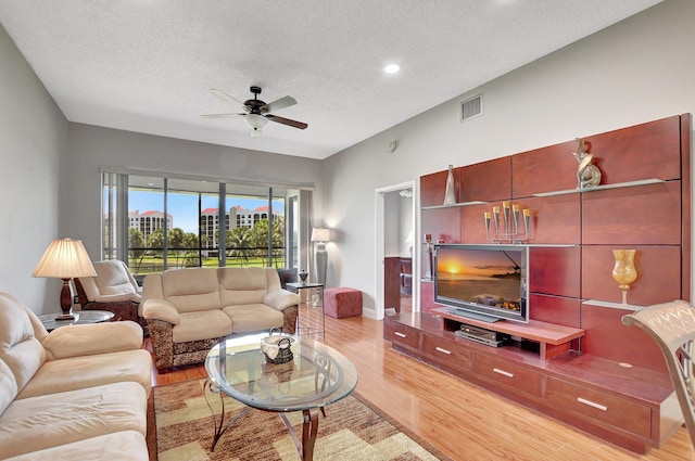 living room with light wood-type flooring, ceiling fan, and a textured ceiling