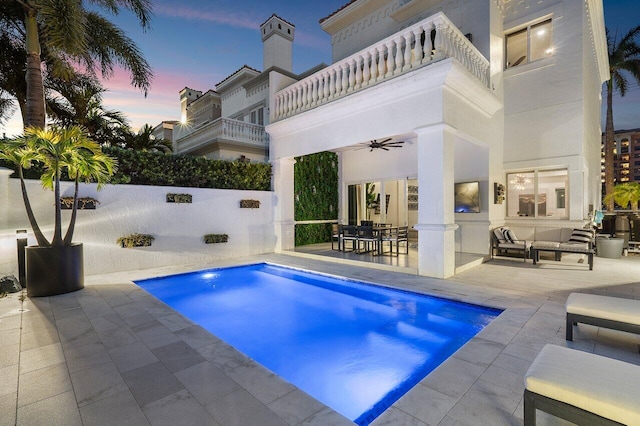 pool at dusk with ceiling fan, an outdoor hangout area, and a patio