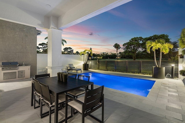 pool at dusk with area for grilling, exterior kitchen, and a patio area