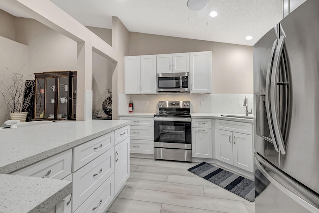 kitchen with appliances with stainless steel finishes, vaulted ceiling, white cabinets, sink, and light wood-type flooring