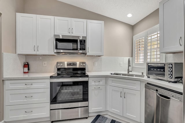 kitchen with stainless steel appliances, lofted ceiling, tasteful backsplash, white cabinetry, and sink