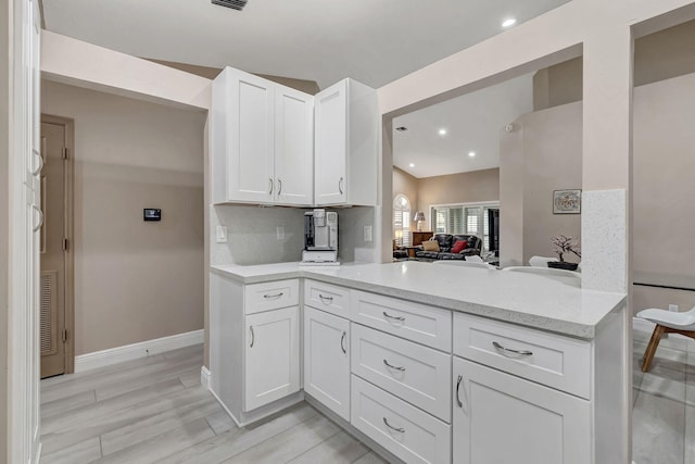 kitchen with backsplash, light wood-type flooring, white cabinetry, kitchen peninsula, and light stone countertops