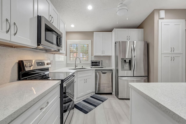 kitchen with stainless steel appliances, light hardwood / wood-style floors, a textured ceiling, white cabinetry, and sink