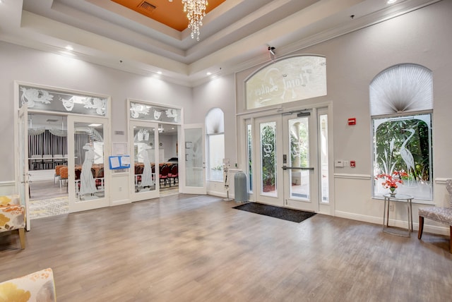 interior space featuring french doors, a high ceiling, hardwood / wood-style flooring, a raised ceiling, and an inviting chandelier