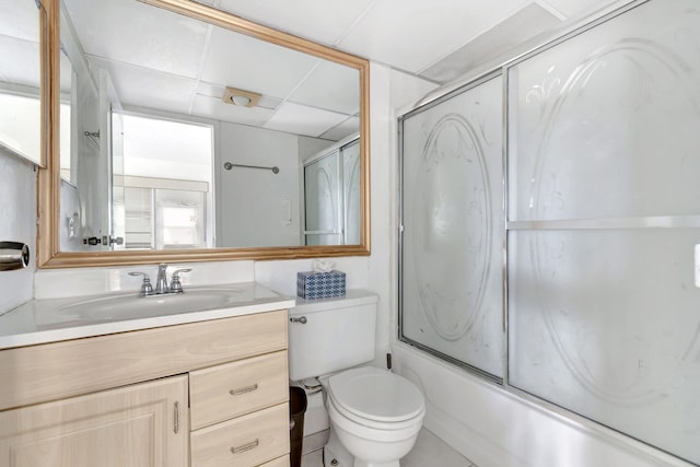 full bathroom with a drop ceiling, toilet, bath / shower combo with glass door, and large vanity