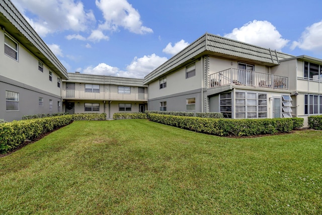 rear view of property featuring a balcony and a yard