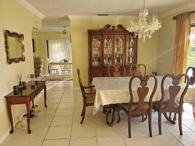 tiled dining room featuring ceiling fan with notable chandelier, a textured ceiling, and ornamental molding