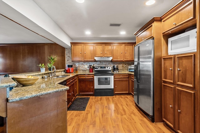 kitchen featuring stainless steel appliances, sink, decorative backsplash, light wood-type flooring, and light stone countertops