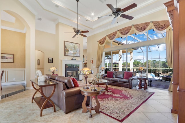 living room with ornamental molding, a towering ceiling, light tile floors, a premium fireplace, and ceiling fan