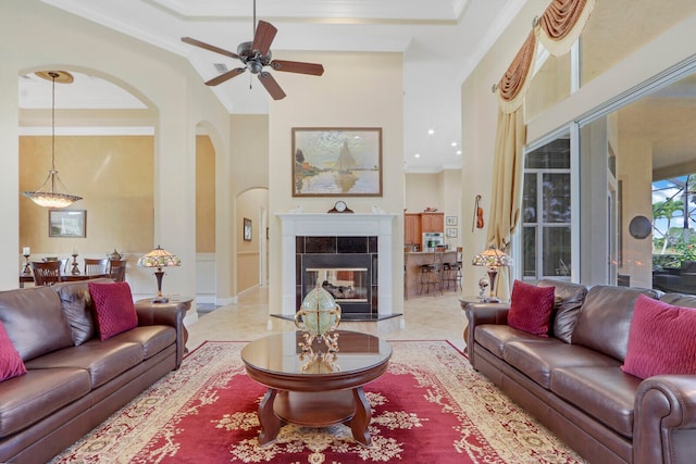 tiled living room with ornamental molding, a towering ceiling, a tiled fireplace, and ceiling fan