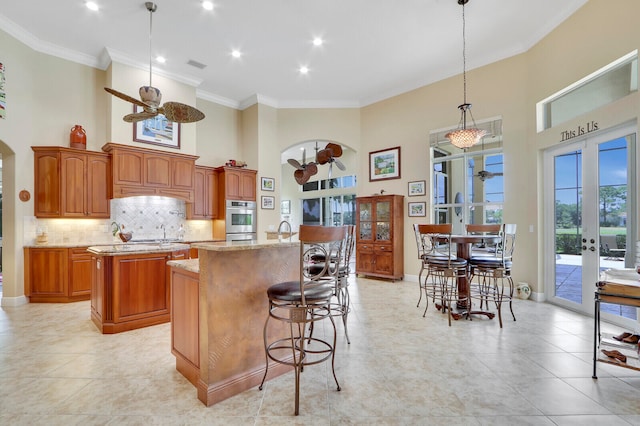 kitchen with french doors, decorative light fixtures, ceiling fan, and a center island with sink