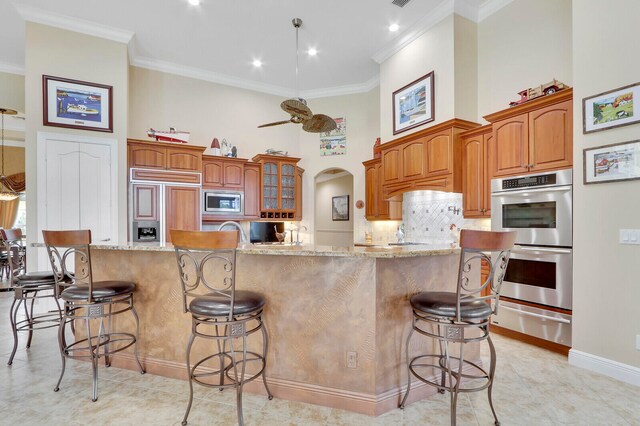 kitchen with ornamental molding, built in appliances, a breakfast bar, and a spacious island