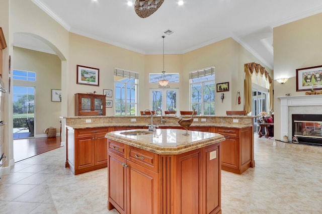 kitchen featuring ornamental molding, a center island with sink, and light stone counters