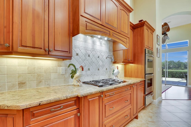 kitchen featuring tasteful backsplash, appliances with stainless steel finishes, light tile floors, and light stone countertops