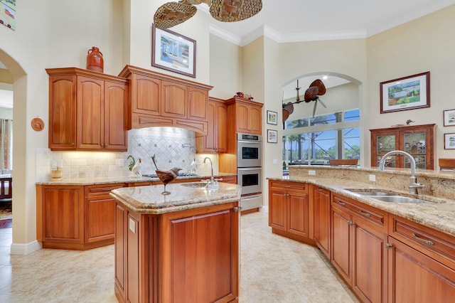 kitchen with a towering ceiling, stainless steel double oven, light stone counters, sink, and light tile floors