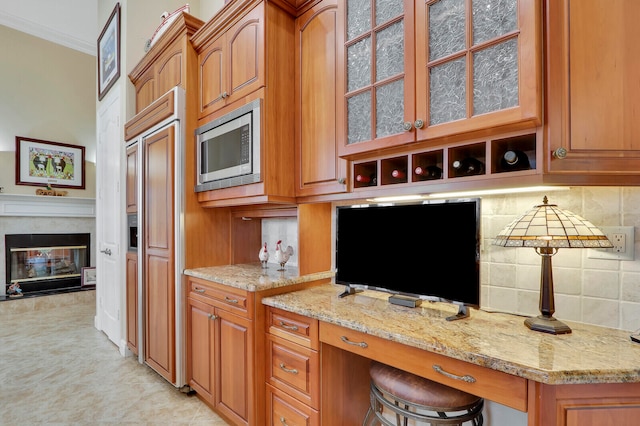 kitchen with built in appliances, light stone countertops, backsplash, a high end fireplace, and a kitchen breakfast bar