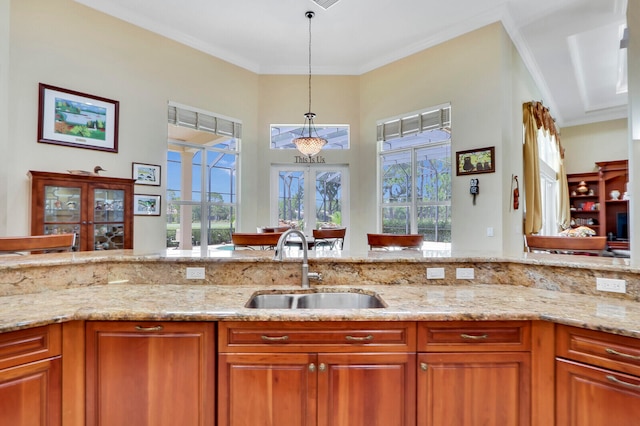 kitchen featuring decorative light fixtures, sink, crown molding, and light stone countertops