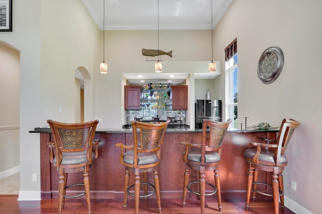 kitchen featuring a towering ceiling, hardwood / wood-style flooring, black refrigerator, and decorative light fixtures