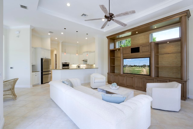 tiled living room with ceiling fan, a tray ceiling, sink, and ornamental molding