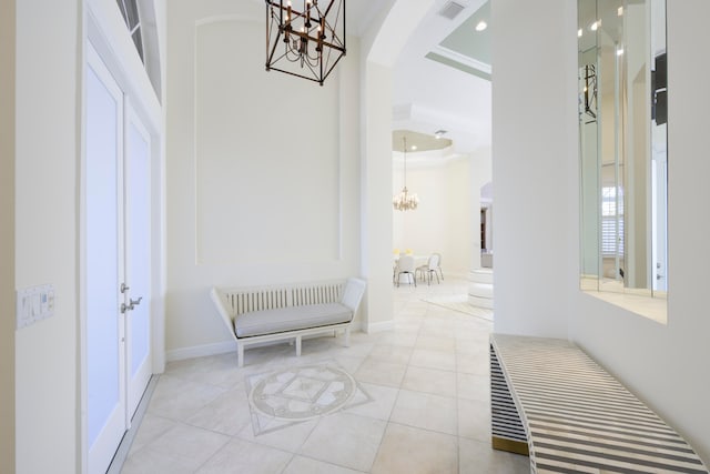 tiled entrance foyer with ornamental molding, an inviting chandelier, and a raised ceiling