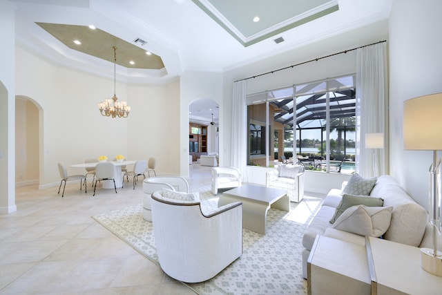 living room with ornamental molding, an inviting chandelier, a tray ceiling, a high ceiling, and light tile floors