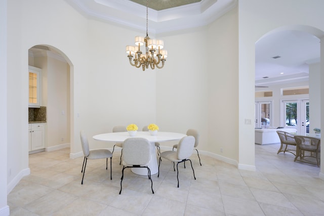 dining space with a raised ceiling, an inviting chandelier, light tile flooring, and french doors