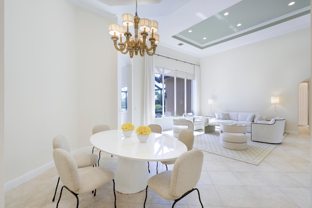 tiled dining room featuring an inviting chandelier, a high ceiling, ornamental molding, and a tray ceiling