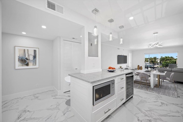 kitchen with light tile floors, a kitchen island, white cabinetry, stainless steel microwave, and hanging light fixtures