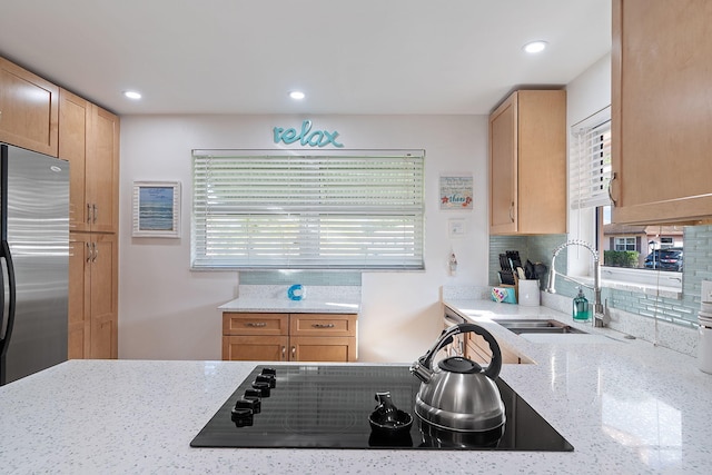 kitchen with stainless steel refrigerator, light stone countertops, sink, and black electric stovetop