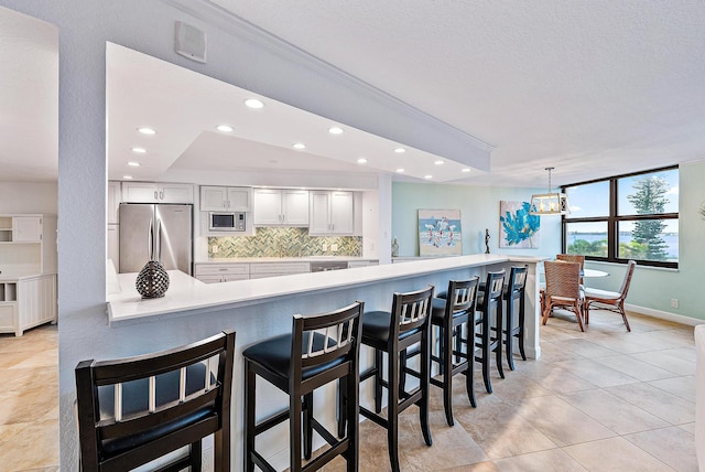 kitchen featuring a kitchen bar, appliances with stainless steel finishes, hanging light fixtures, tasteful backsplash, and white cabinetry