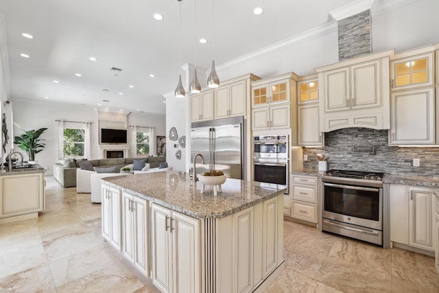 kitchen with hanging light fixtures, an island with sink, stainless steel appliances, and cream cabinetry