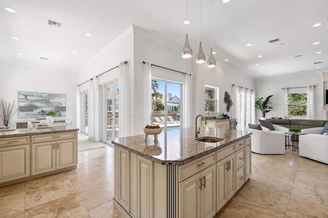 kitchen featuring light stone countertops, sink, an island with sink, decorative light fixtures, and cream cabinetry