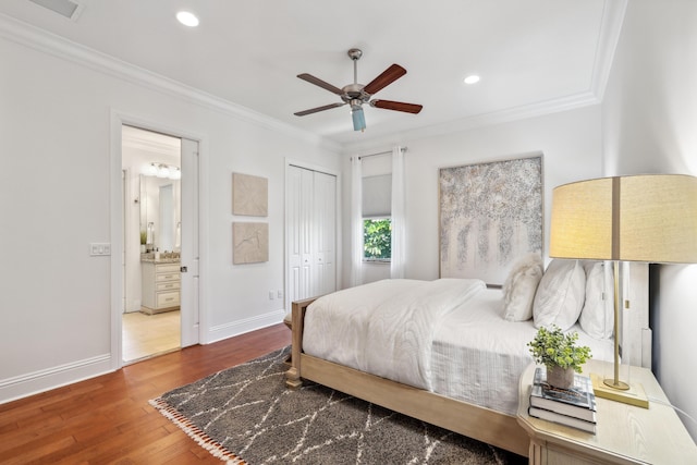 bedroom featuring crown molding, ensuite bath, hardwood / wood-style flooring, ceiling fan, and a closet