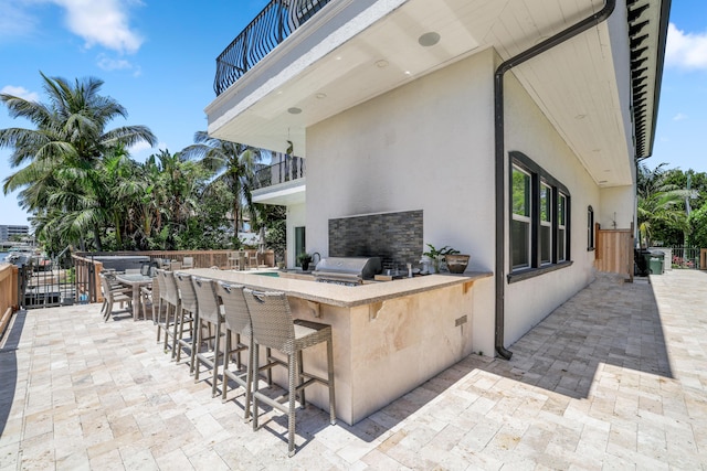 view of patio featuring exterior bar, an outdoor kitchen, a balcony, and a grill