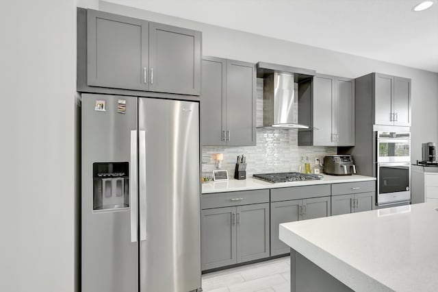 kitchen featuring gray cabinetry, appliances with stainless steel finishes, tasteful backsplash, and wall chimney range hood