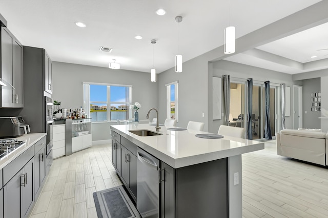 kitchen with stainless steel appliances, a kitchen island with sink, sink, and hanging light fixtures