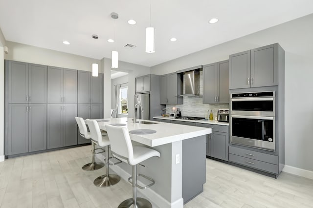 kitchen featuring appliances with stainless steel finishes, gray cabinetry, wall chimney range hood, and pendant lighting