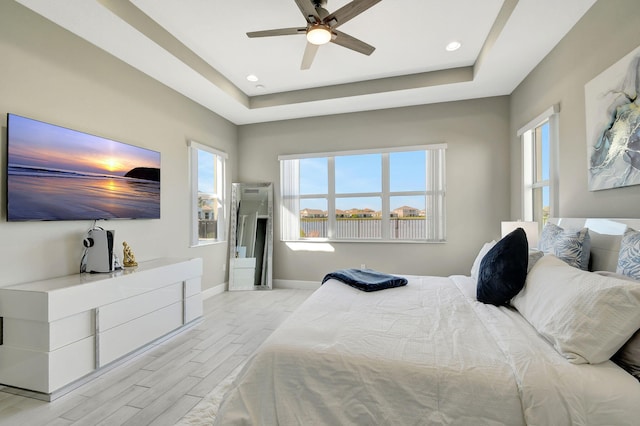 bedroom featuring multiple windows, light hardwood / wood-style floors, a raised ceiling, and ceiling fan