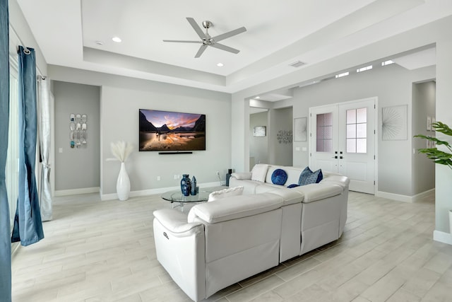 living room featuring a raised ceiling, ceiling fan, and french doors