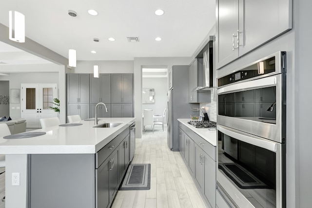 kitchen featuring pendant lighting, sink, gray cabinets, appliances with stainless steel finishes, and an island with sink