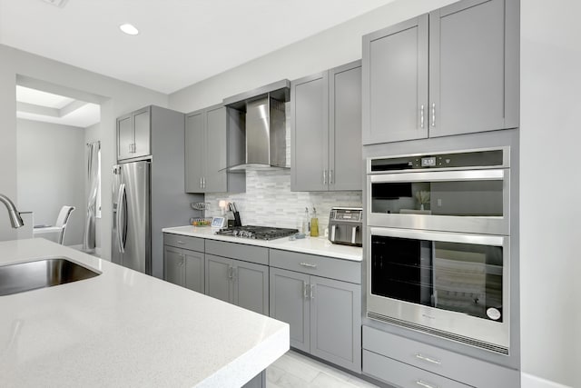 kitchen featuring sink, gray cabinetry, appliances with stainless steel finishes, wall chimney range hood, and backsplash