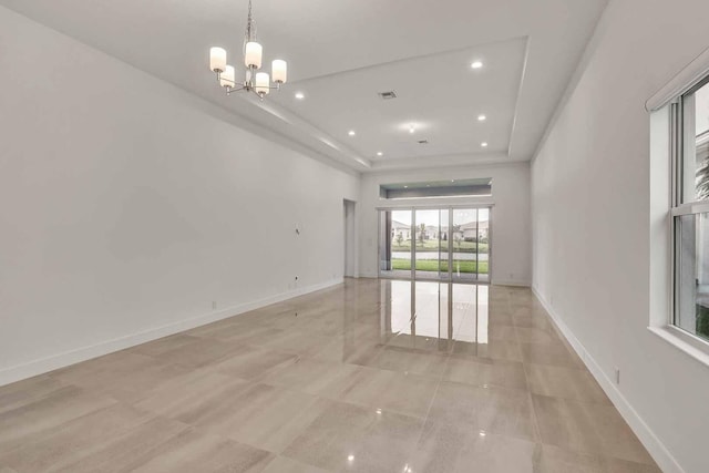 spare room with an inviting chandelier, a raised ceiling, and light tile patterned flooring