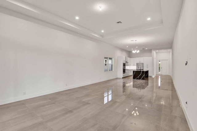 unfurnished living room featuring a raised ceiling and a chandelier