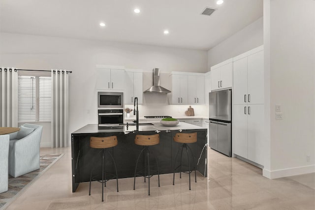 kitchen featuring wall chimney exhaust hood, stainless steel appliances, a breakfast bar area, and white cabinets