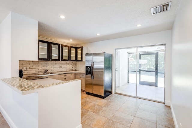 kitchen with a textured ceiling, sink, light tile flooring, tasteful backsplash, and stainless steel fridge