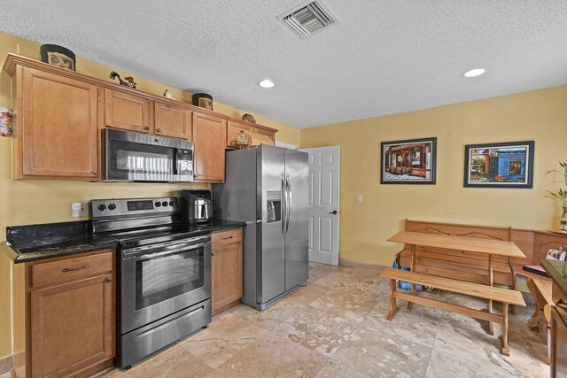 kitchen with stainless steel appliances, dark stone countertops, and a textured ceiling