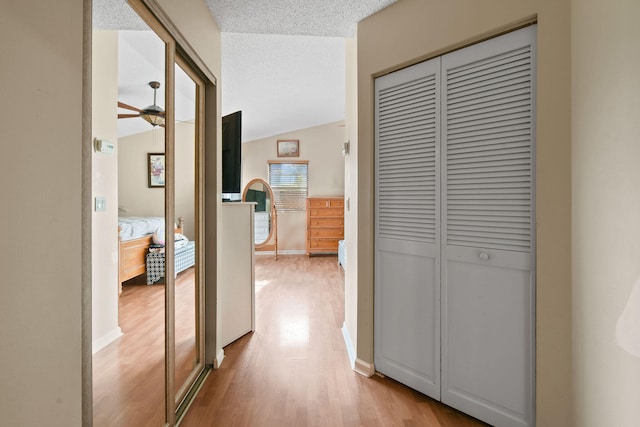 hallway featuring a textured ceiling, light wood-type flooring, and vaulted ceiling