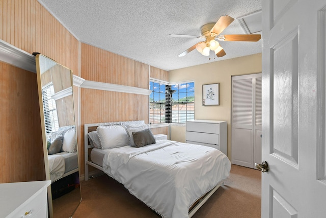 bedroom with ceiling fan, a textured ceiling, wooden walls, a closet, and light colored carpet